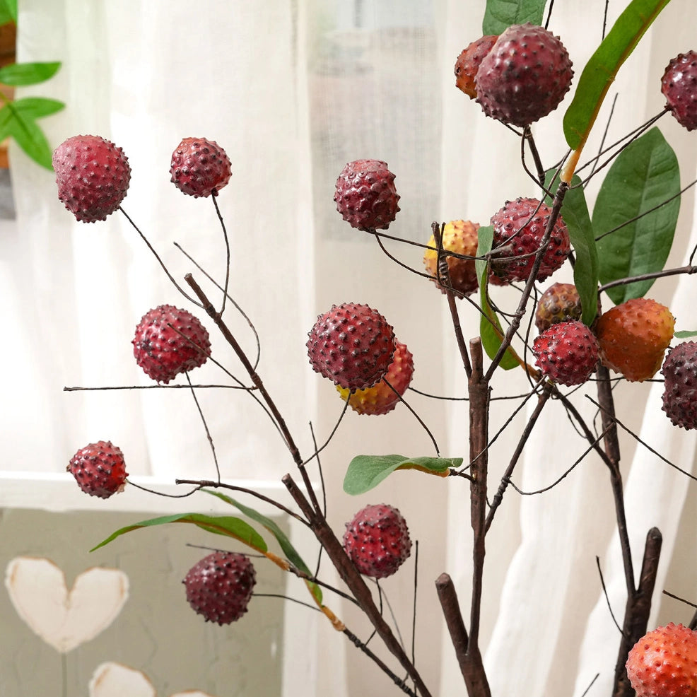 Close up of lifelike artificial lychee fruit branches with textured red faux berries and leaves