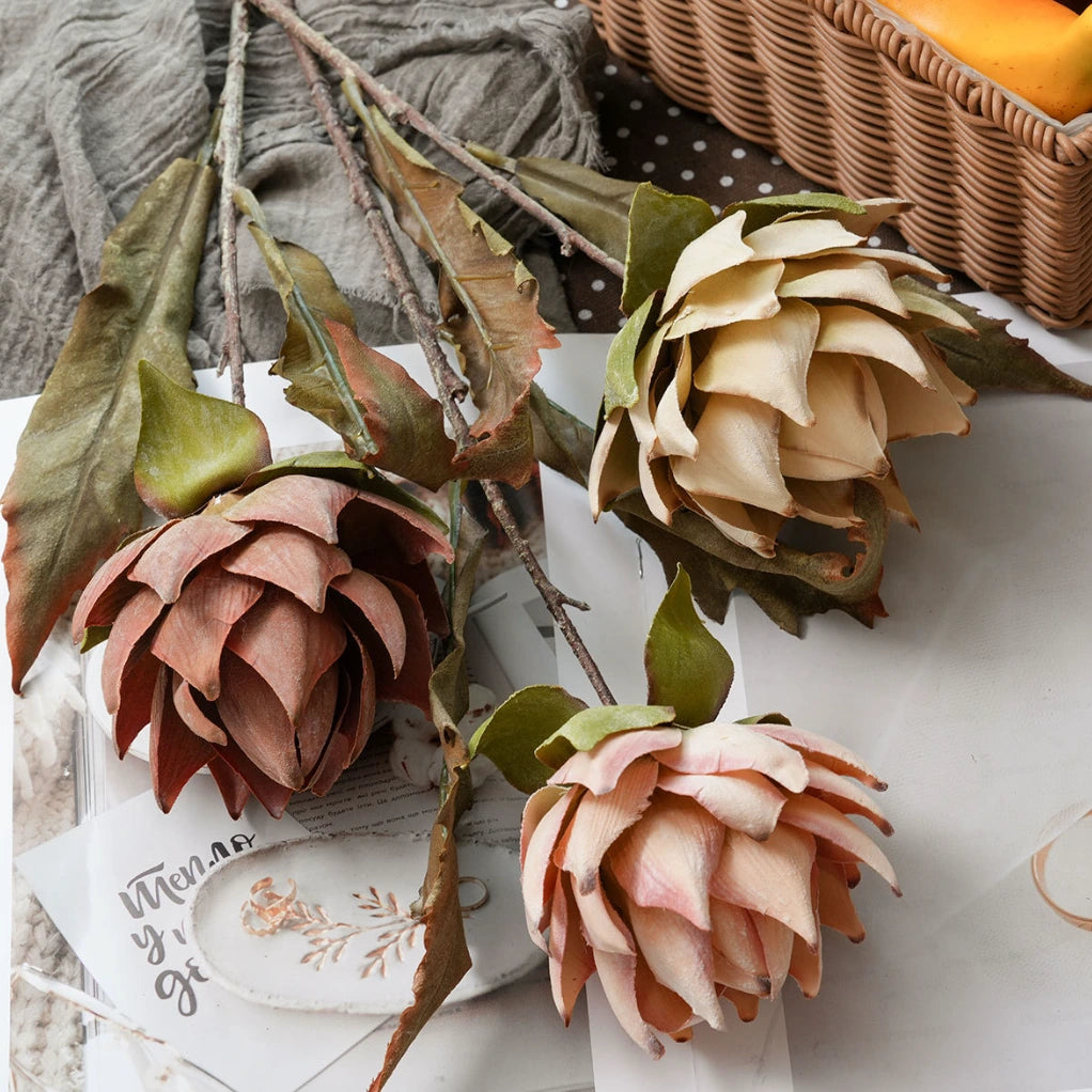 Artificial protea flower stems arranged on fabric with vintage aesthetic floral decor