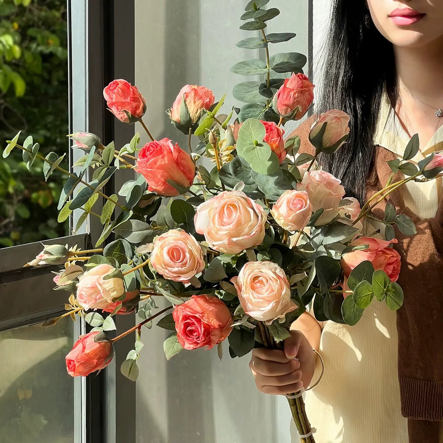 Woman holding artificial rose bouquet with eucalyptus in soft blush tones near window