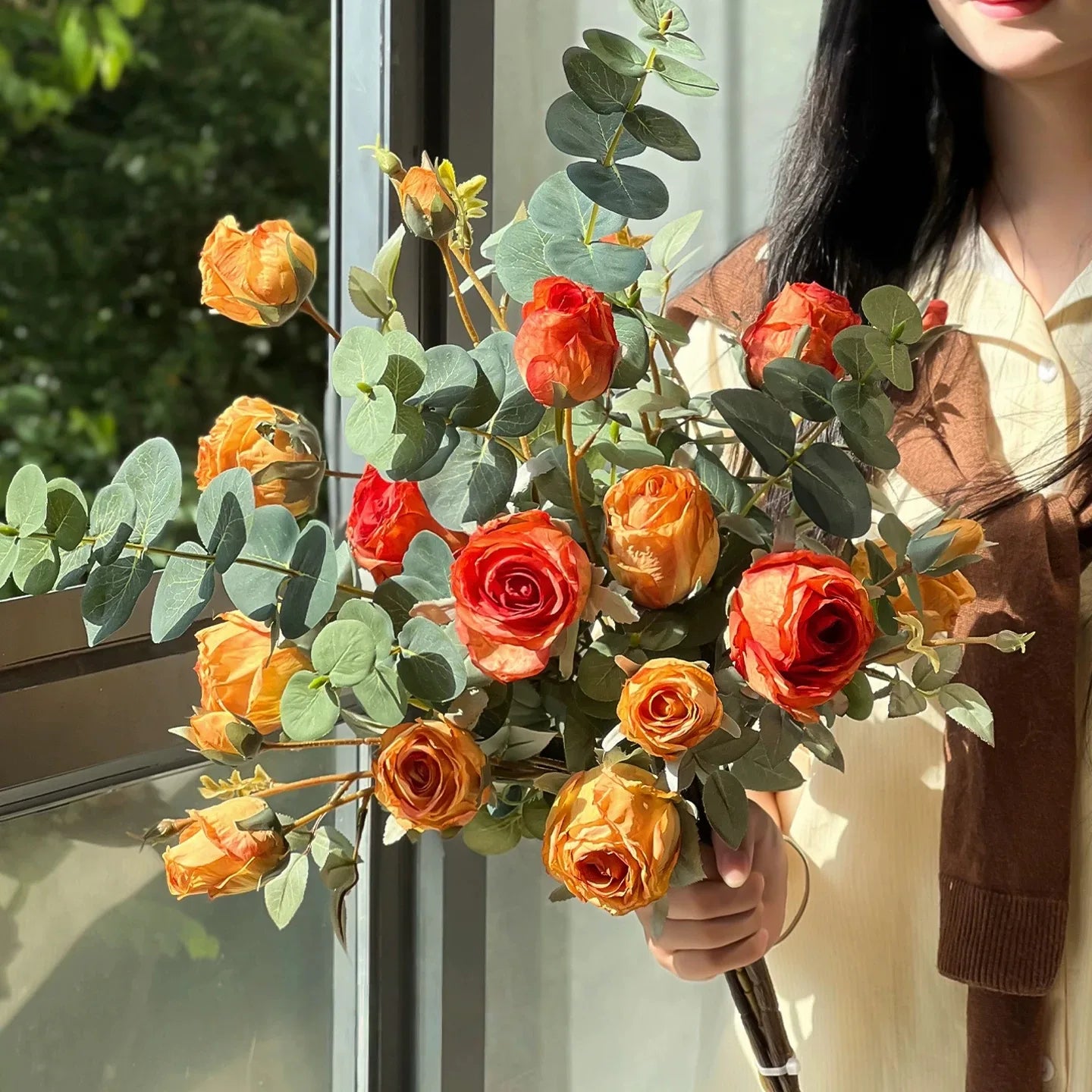 Handheld artificial rose bouquet with eucalyptus in warm orange and amber tones