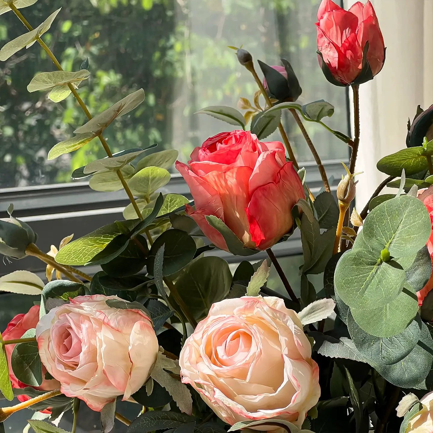 Close-up of realistic artificial roses with layered petals and eucalyptus leaves