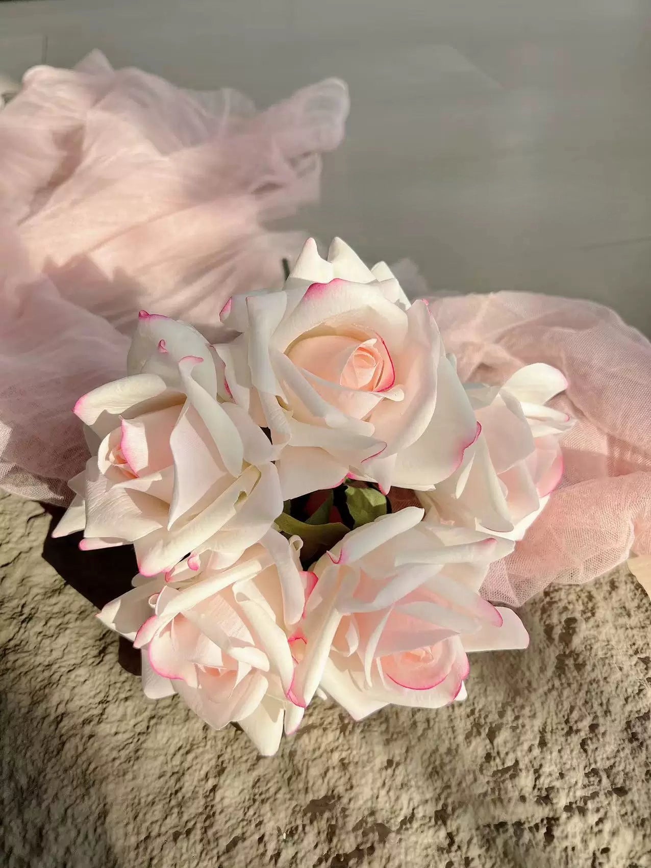 White artificial roses with pink edges styled on soft fabric